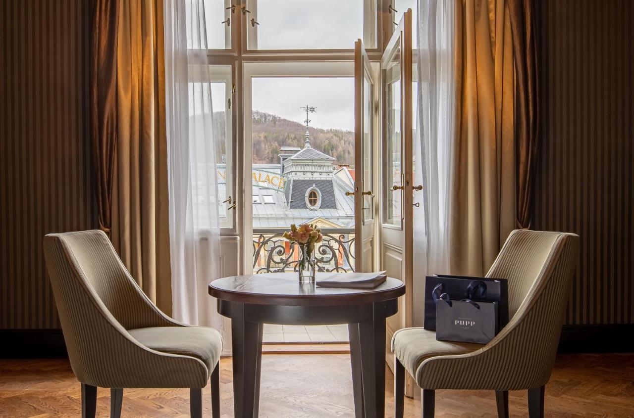 แกรนด์โฮเต็ล พัปป์ Hotel การ์โลวีวารี ภายนอก รูปภาพ The photo depicts a cozy interior setting, likely within a hotel room or a private space. There are two elegant chairs positioned around a round wooden table. On the table, there is a small vase with flowers, adding a touch of warmth to the environme