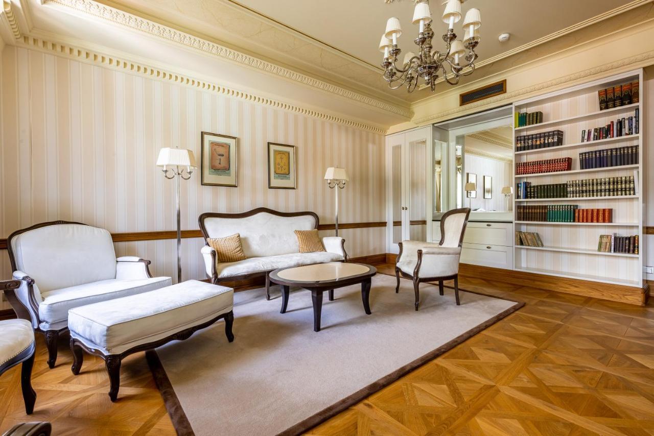 แกรนด์โฮเต็ล พัปป์ Hotel การ์โลวีวารี ภายนอก รูปภาพ The photo shows a spacious and elegantly designed living room. It features a light color palette with subtle striped wallpaper. In the center, there is a round coffee table surrounded by two armchairs and a modest sofa, all in a classic style. A chan