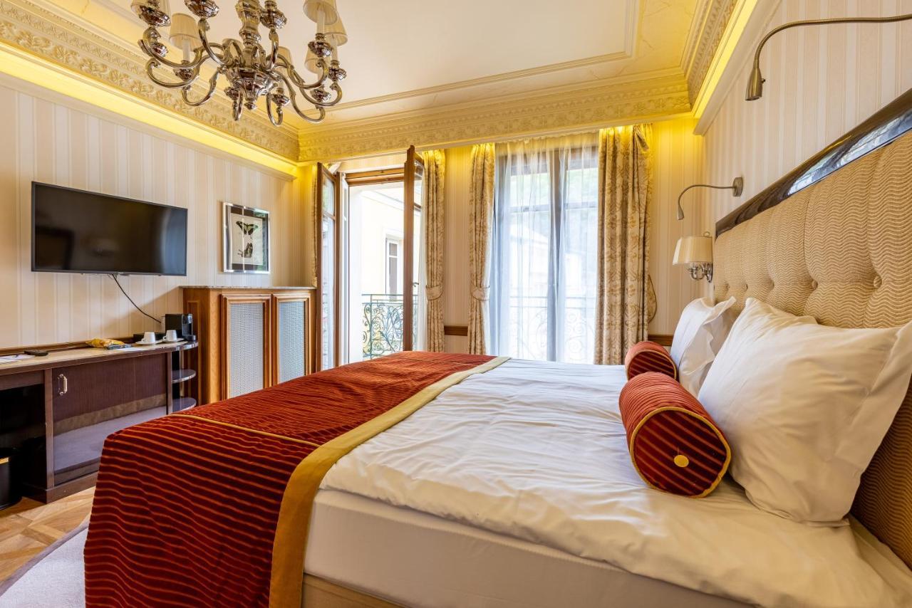 แกรนด์โฮเต็ล พัปป์ Hotel การ์โลวีวารี ภายนอก รูปภาพ The photo shows an elegant bedroom designed with a warm and inviting ambiance. There is a large bed dressed in white linens and accented with a rich red bedspread. Two decorative pillows are placed at the head of the bed, adding to the room's sophist