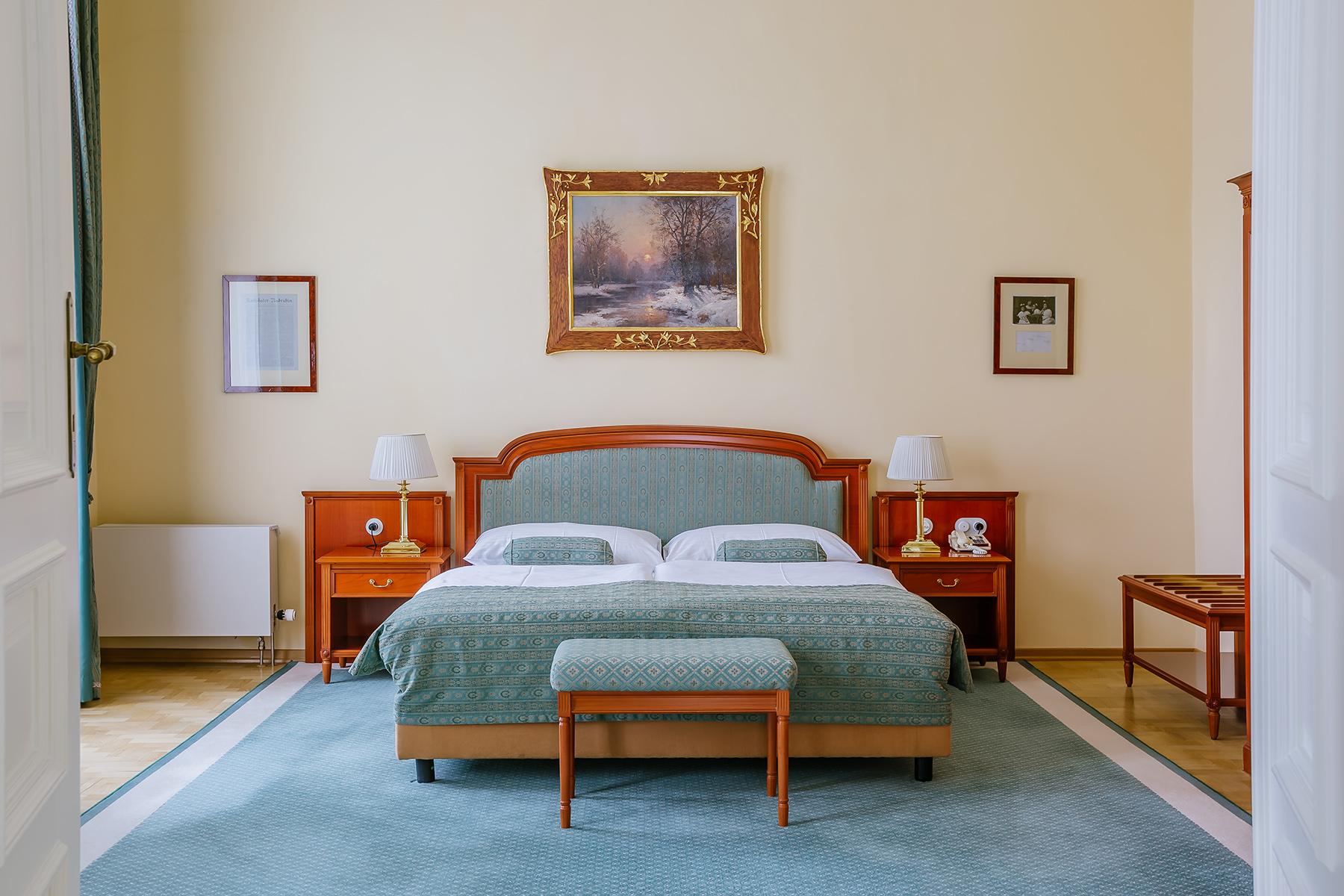แกรนด์โฮเต็ล พัปป์ Hotel การ์โลวีวารี ภายนอก รูปภาพ The photo shows a cozy bedroom with a light-colored wall. There is a large bed with a muted green coverlet and white bedding. On either side of the bed, there are bedside tables with lamps. At the foot of the bed, there is a small bench. Above the be