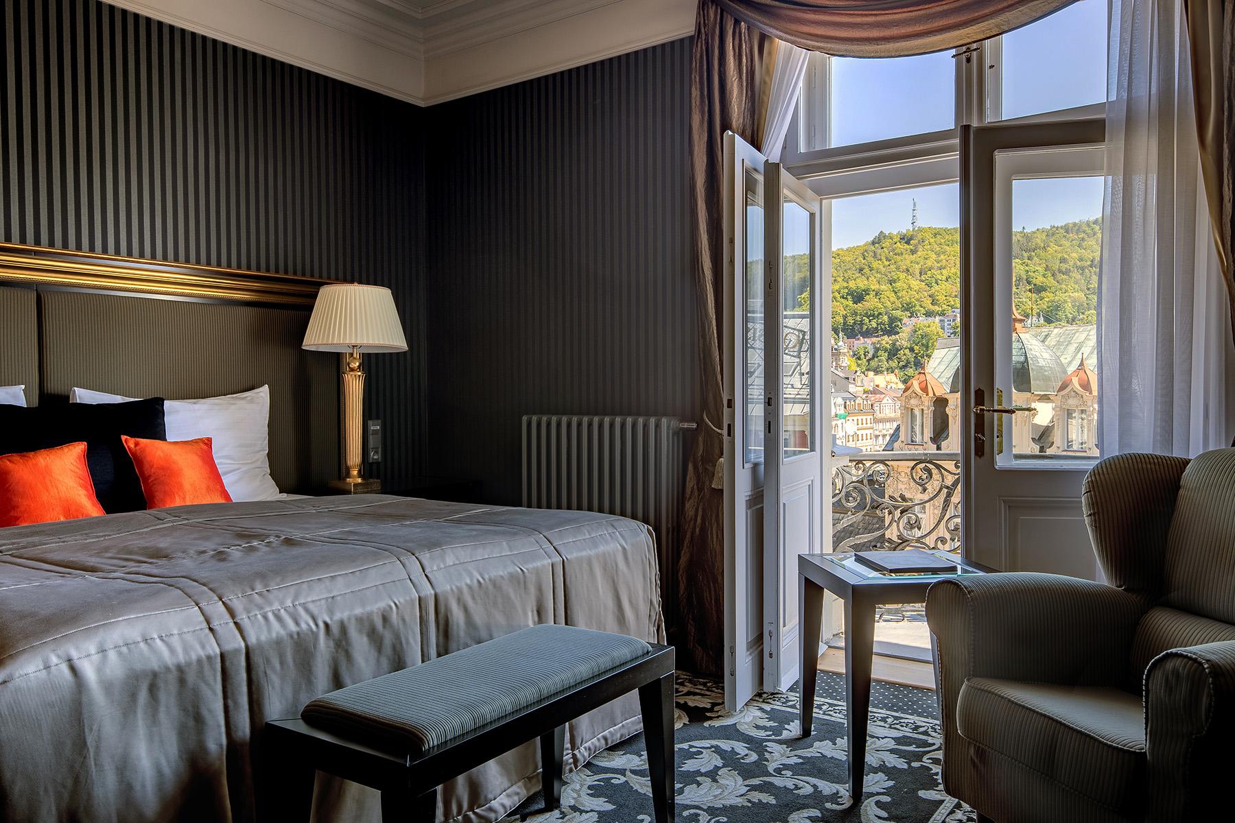 แกรนด์โฮเต็ล พัปป์ Hotel การ์โลวีวารี ภายนอก รูปภาพ The photo shows a cozy hotel room with a sophisticated design. The room features a bed with a plush grey duvet and decorative pillows in black and orange. There is a bedside lamp beside the bed. A comfortable armchair sits in one corner. The room has