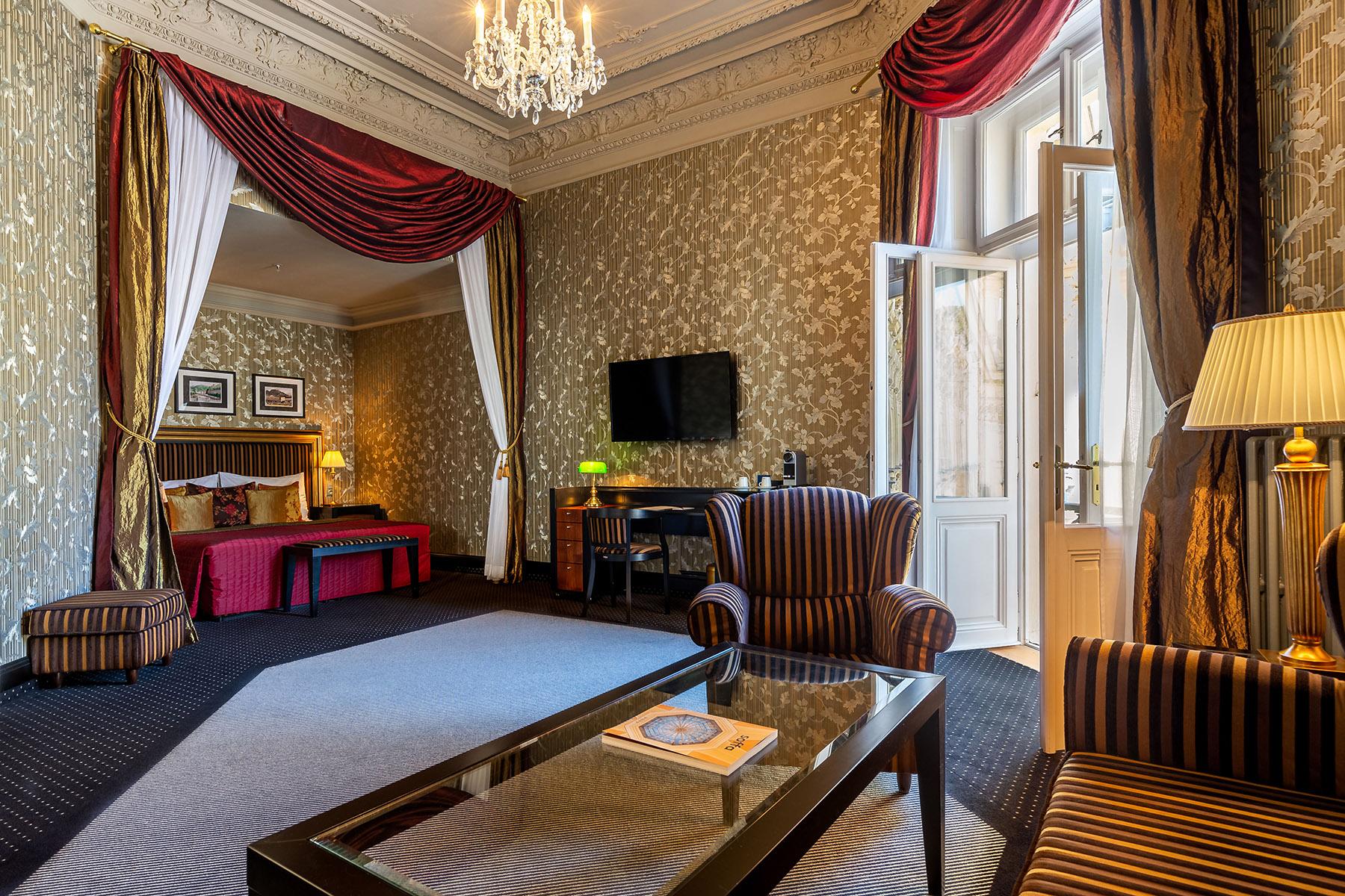 แกรนด์โฮเต็ล พัปป์ Hotel การ์โลวีวารี ภายนอก รูปภาพ The photo shows a luxurious hotel room featuring elegant decor. The room has tall windows with flowing curtains, a plush carpet, and ornate wallpaper. There are two comfortable armchairs with a stylish design positioned around a glass coffee table. A