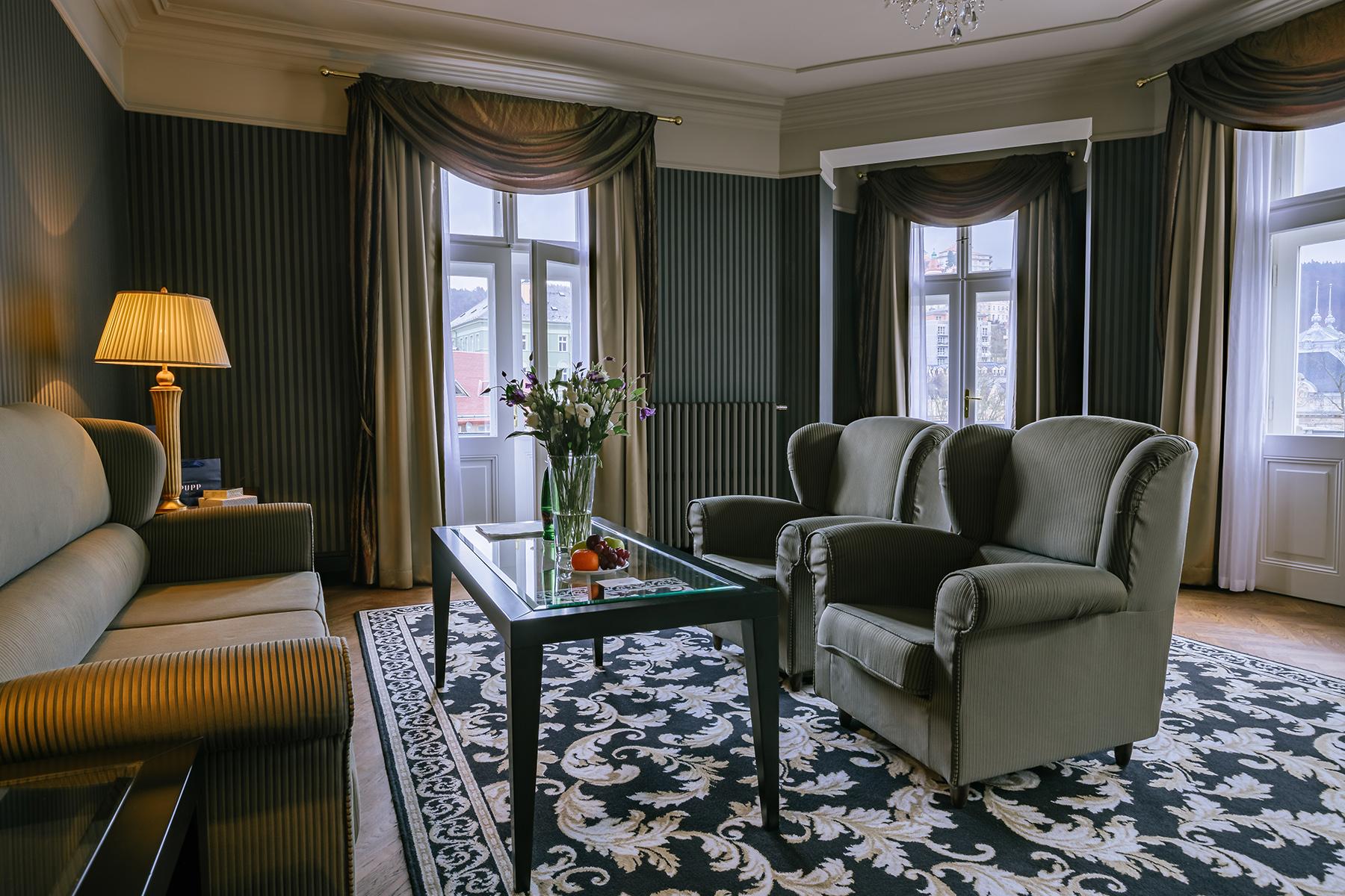 แกรนด์โฮเต็ล พัปป์ Hotel การ์โลวีวารี ภายนอก รูปภาพ The photo shows a cozy living room with a warm and elegant decor. It features two green upholstered armchairs and a beige sofa. In the center, there’s a glass coffee table with a small vase of flowers. The room is enhanced by dark wallpaper and soft 