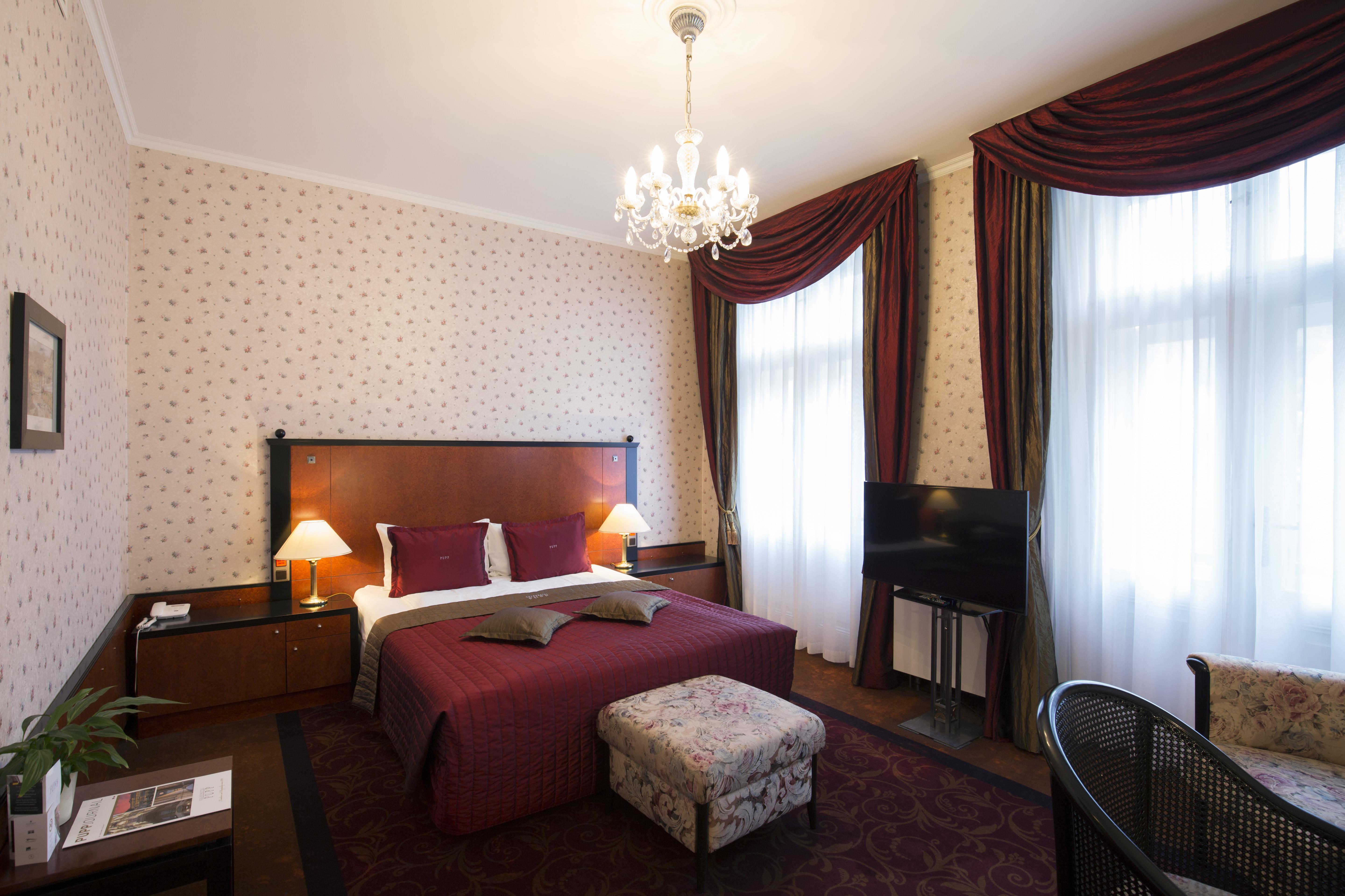 แกรนด์โฮเต็ล พัปป์ Hotel การ์โลวีวารี ภายนอก รูปภาพ The photo shows a cozy hotel room with a double bed dressed in rich red bedding and two purple decorative pillows. The walls are adorned with a tasteful patterned wallpaper. There are two elegant windows with heavy, dark curtains that let in natural 