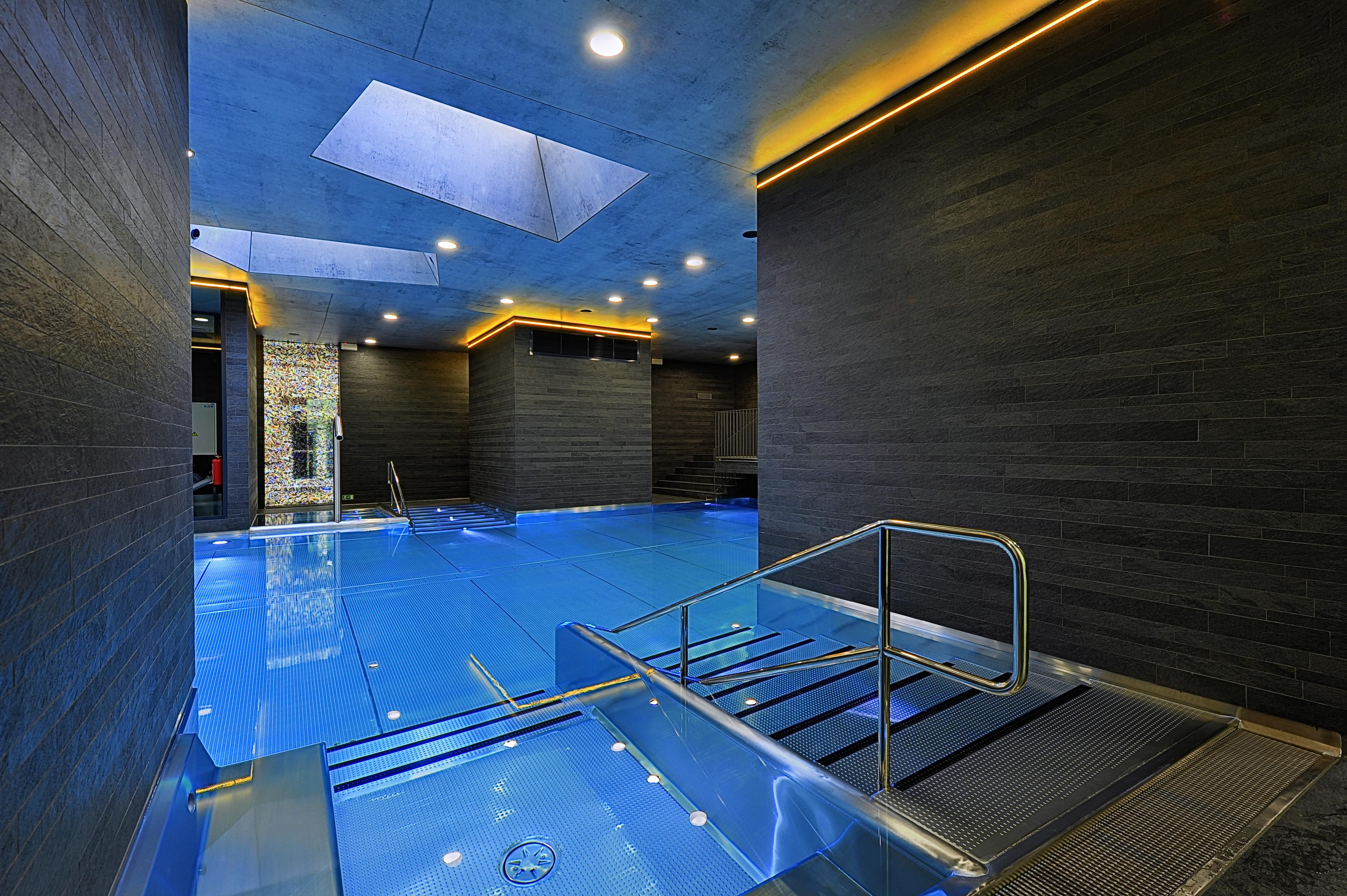 แกรนด์โฮเต็ล พัปป์ Hotel การ์โลวีวารี ภายนอก รูปภาพ The photo features a modern indoor swimming pool area. The pool is designed with a sleek, contemporary aesthetic, featuring a vibrant blue water surface. The surrounding walls are made of dark materials, possibly stone or wood, complemented by warm l