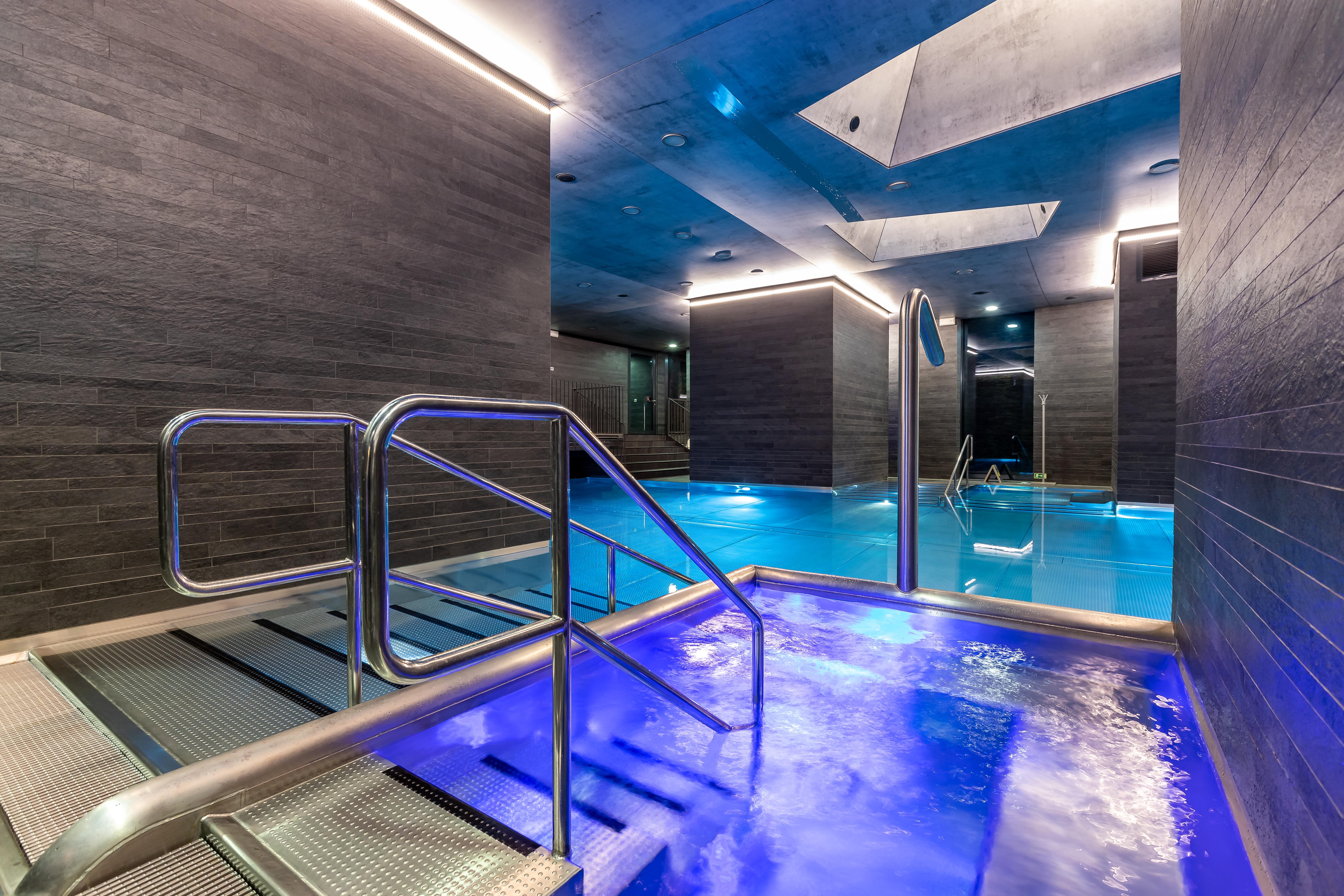 แกรนด์โฮเต็ล พัปป์ Hotel การ์โลวีวารี ภายนอก รูปภาพ The photo shows a modern spa area with a pool. There are sleek, dark walls and blue lighting that creates a tranquil atmosphere. A metal railing leads down into the pool, which has a section with bubbling water. The overall design features clean line