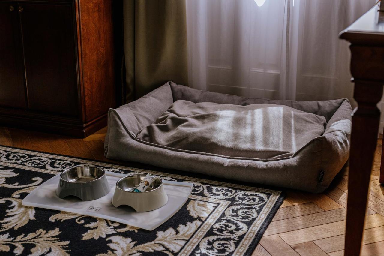แกรนด์โฮเต็ล พัปป์ Hotel การ์โลวีวารี ภายนอก รูปภาพ The photo shows a cozy pet area inside a room. There is a soft, rectangular pet bed in a muted color, positioned against a wall, with some light filtering through a window. In front of the bed, there are two pet bowls placed on a mat, one bowl is gre