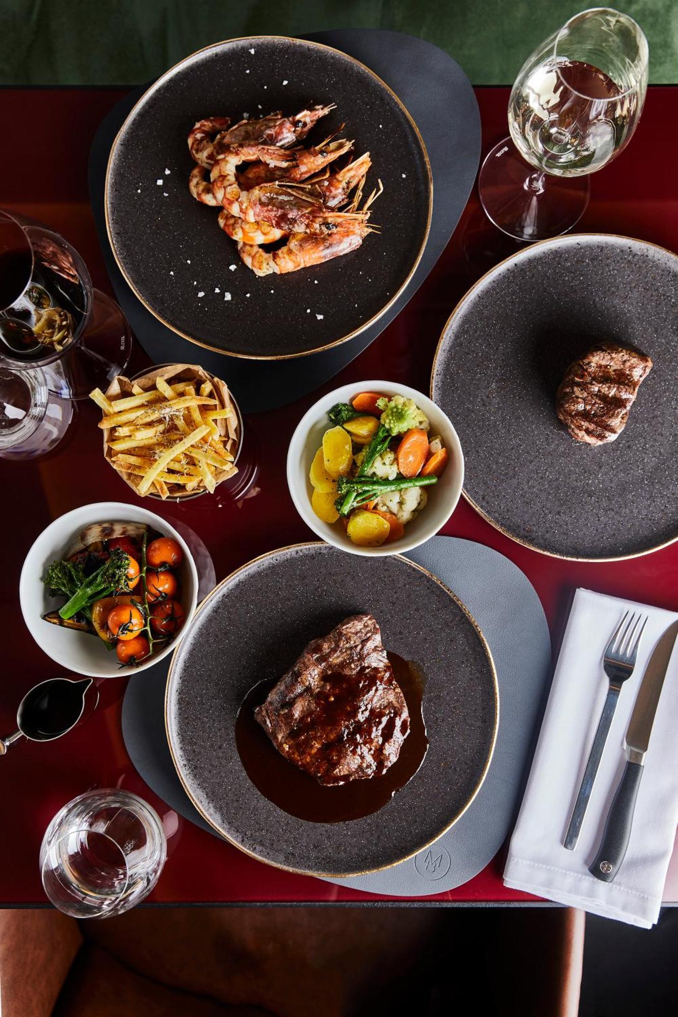 แกรนด์โฮเต็ล พัปป์ Hotel การ์โลวีวารี ภายนอก รูปภาพ The photo features a gourmet meal spread across a dining table. Key elements include:

1. **Main Dishes**: There are two pieces of grilled steak, one prominently displayed at the bottom and another slightly obscured at the top right, both garnished w