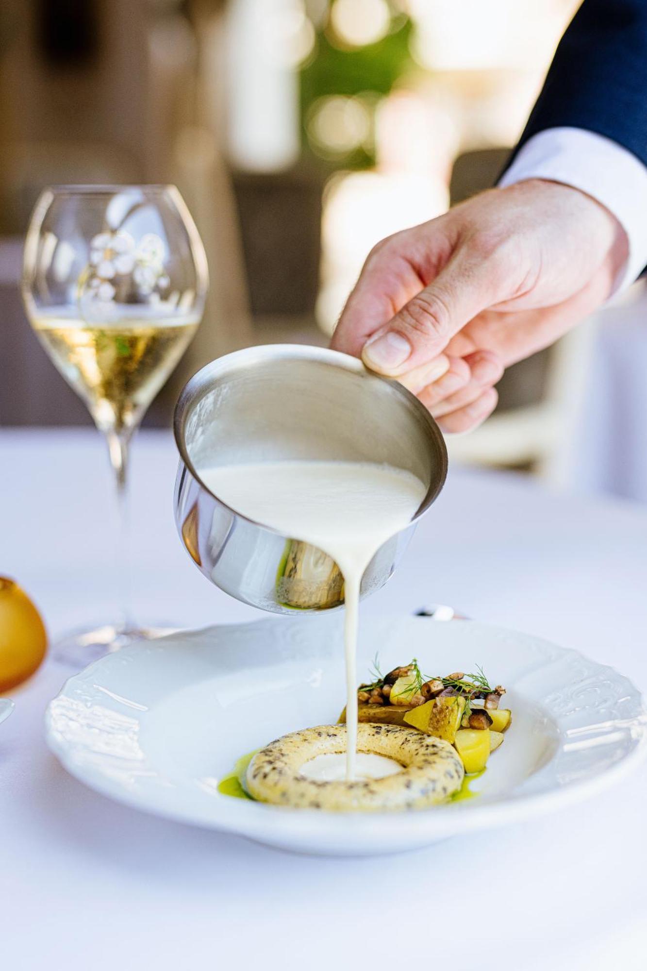 แกรนด์โฮเต็ล พัปป์ Hotel การ์โลวีวารี ภายนอก รูปภาพ The photo shows a hand pouring a creamy sauce from a small stainless steel container over a plated dish, which appears to include vegetables and possibly pasta. In the background, there's a glass of sparkling wine, suggesting a fine dining setting. T
